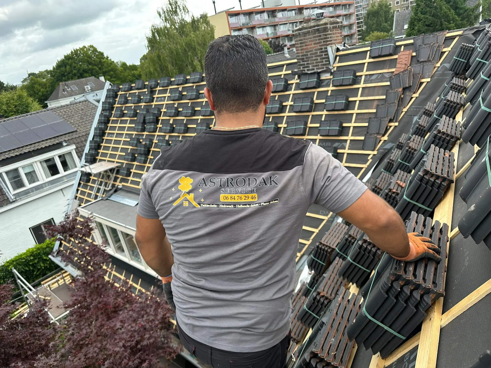 Dakdekker met Astrodak Service shirt op een hellend dak in aanbouw met stapels dakpannen op de panlatten