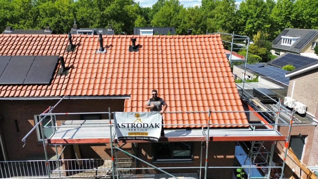 Woning met rood pannendak en steiger met Astrodak Service spandoek tijdens dakwerkzaamheden, met zonnepanelen op het dak