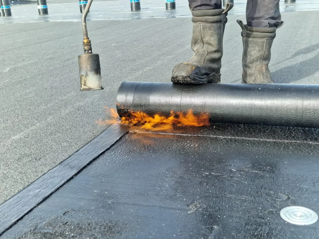 Dakdekker brandt een rol bitumen dakbedekking aan met een gasbrander op een plat dak