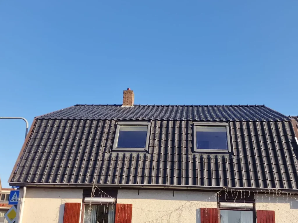 Woning met dak met antracieten dakpannen en twee dakramen onder een blauwe lucht