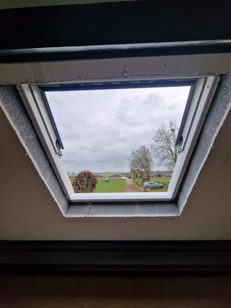 Geopend dakraam van binnenuit gezien met uitzicht op een landelijk landschap