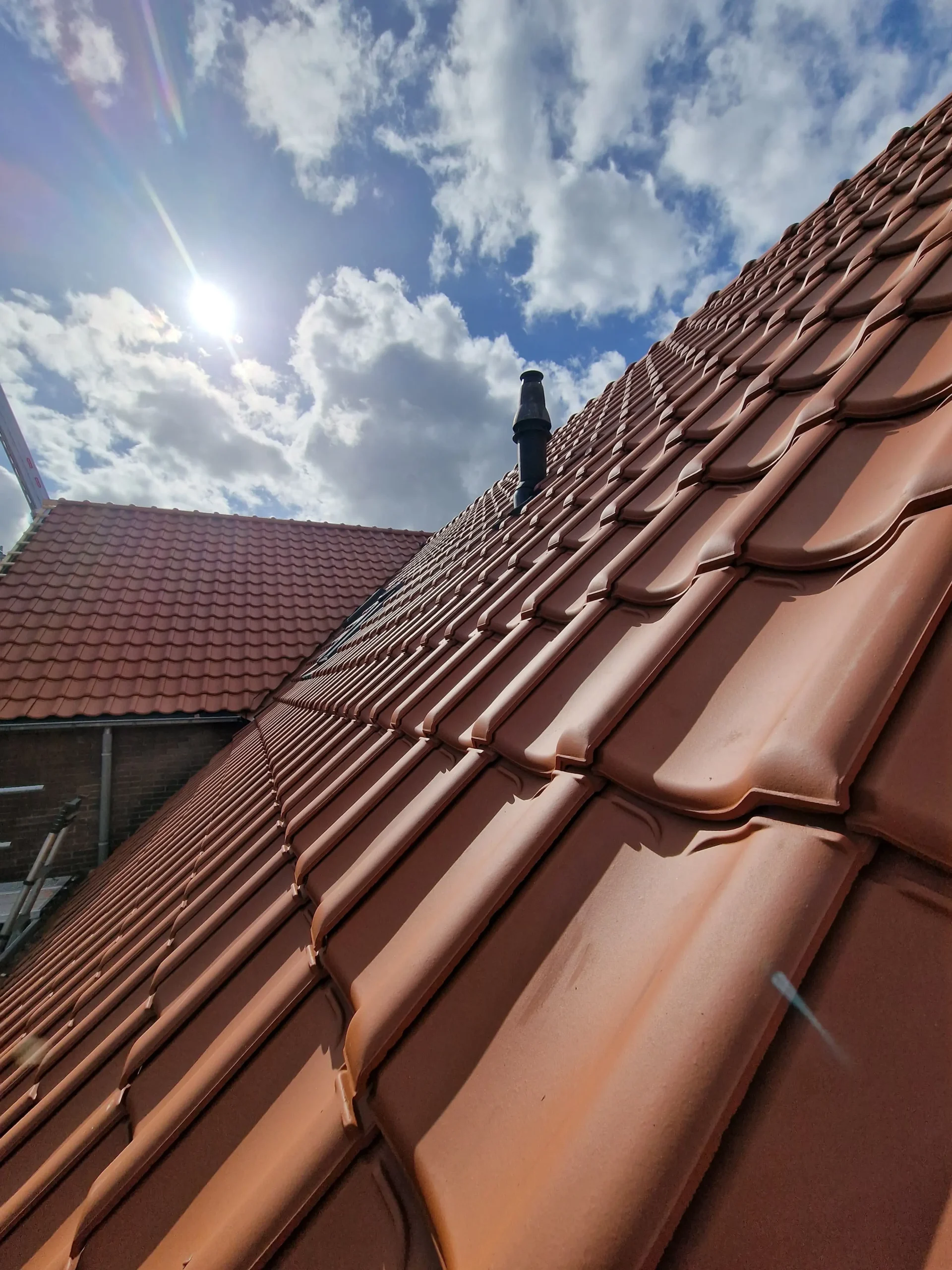 Dak met nieuwe rode dakpannen en een dakdoorvoer tegen een zonnige lucht