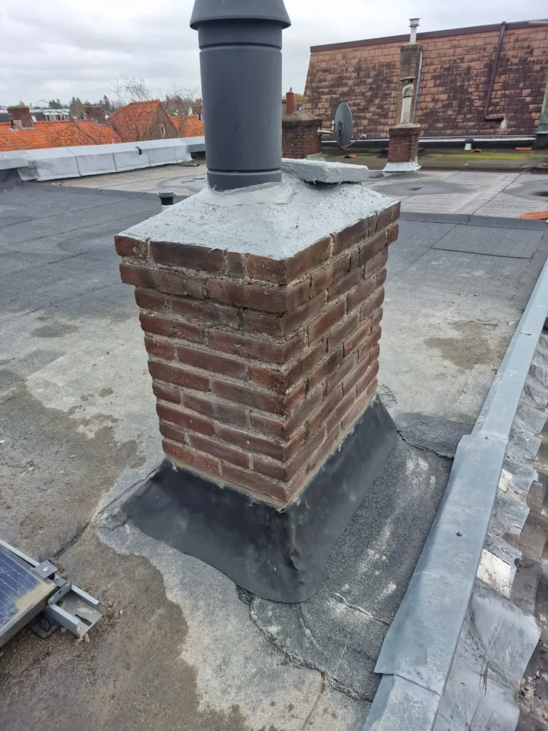 Gemetselde schoorsteen met betonnen deksel en nieuw loodwerk op een plat dak met zonnepanelen
