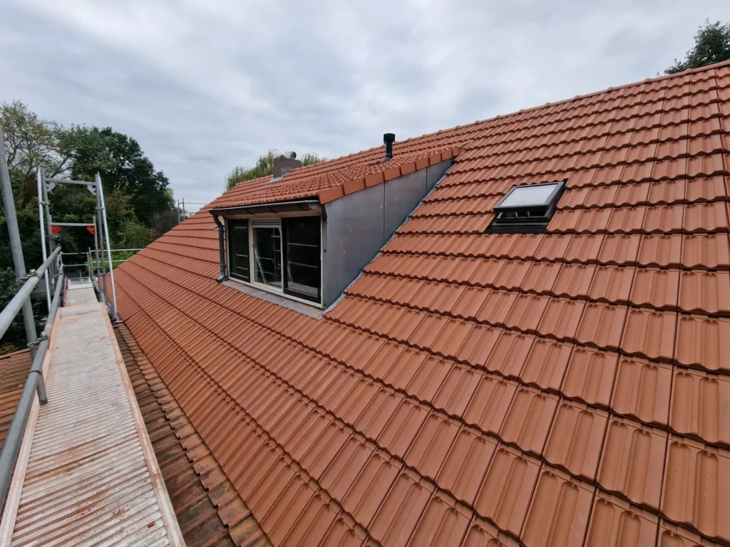 Hellend dak met rode dakpannen, een zinken dakkapel en dakramen tijdens dakwerk