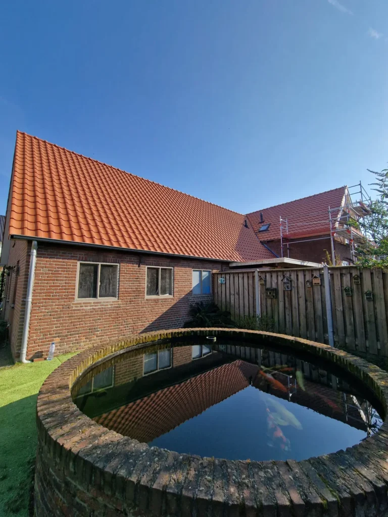 Woning met nieuw dak met rode dakpannen en een ronde koivijver in de tuin