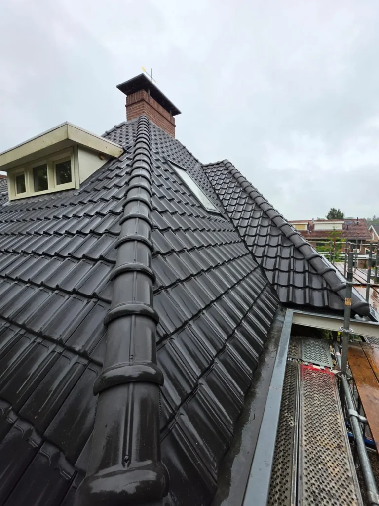 Hellend dak met glanzende zwarte dakpannen, nokvorsten, dakkapel en gemetselde schoorsteen