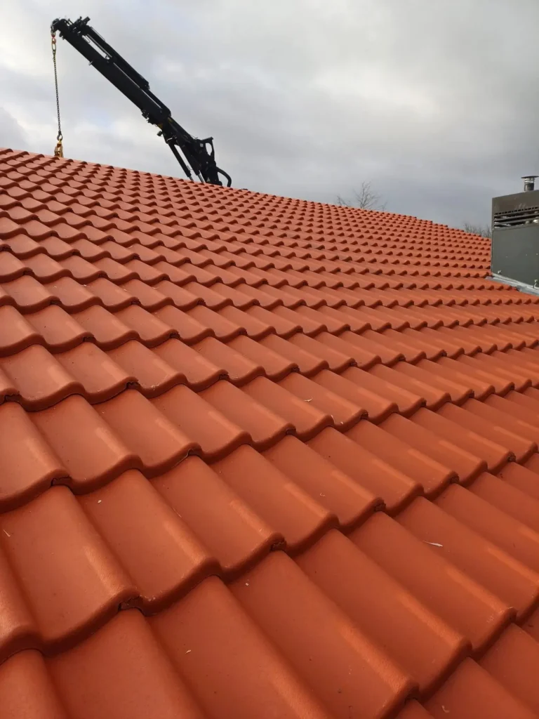 Nieuw gedekt dak met rode dakpannen en een kraan op de achtergrond tijdens dakproject