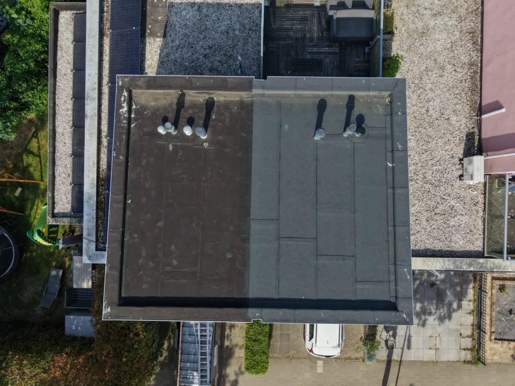 Luchtfoto met drone van een plat dak op een woning met dakdoorvoeren, omgeven door tuin