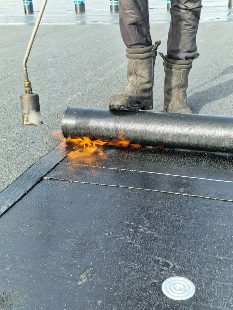 Dakdekker brandt bitumineuze dakbedekking aan met een gasbrander op een plat dak