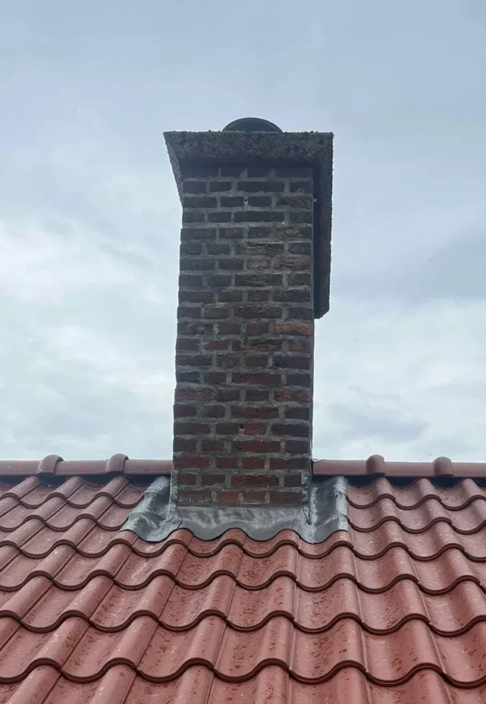 Gemetselde schoorsteen op een rood pannendak met nieuw loodwerk rondom de voet, project in Den Dungen