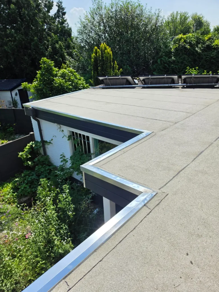 Plat dak met lichte dakbedekking en metalen daktrim langs de rand, omgeven door groen, project in Vught