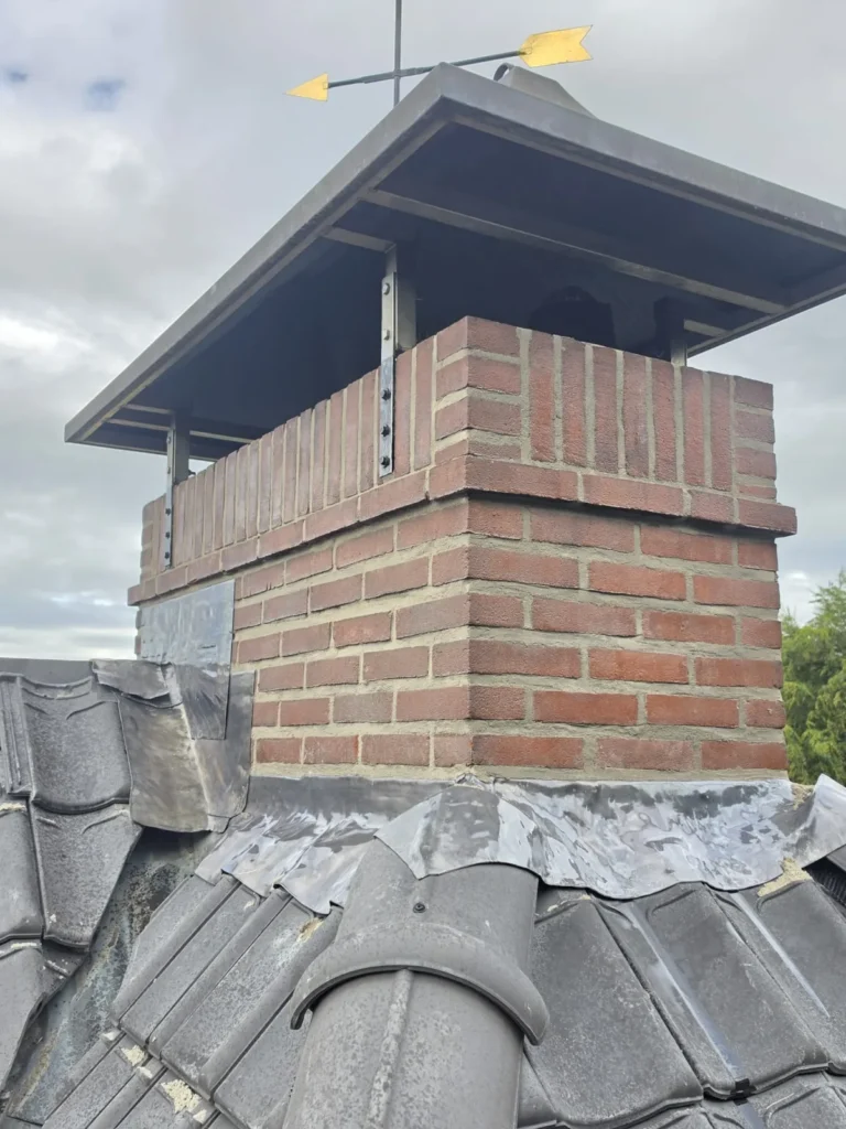 Nieuw gemetselde schoorsteen met metalen regenkap en windwijzer op een dak, project in Malden