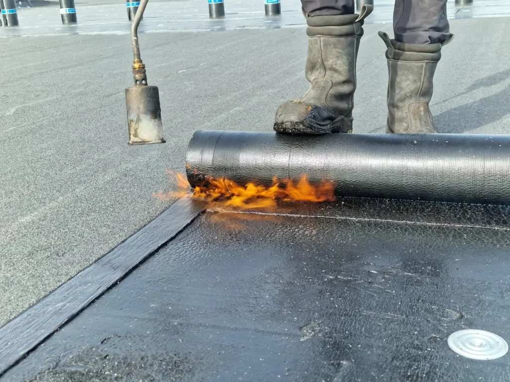 Dakdekker brandt met een gasbrander een rol bitumen dakbedekking aan op een plat dak bij het verhelpen van een daklekkage