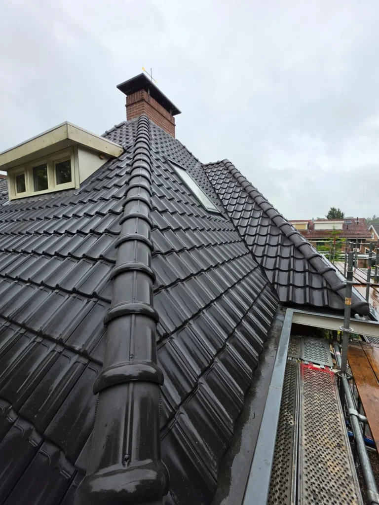 Hellend dak met nieuwe antracietkleurige dakpannen, schoorsteen en dakkapel met steiger langs de zijkant