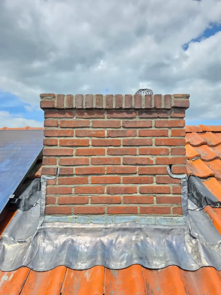 Rode bakstenen schoorsteen met nieuw loodwerk op een dak met rode dakpannen en zonnepanelen